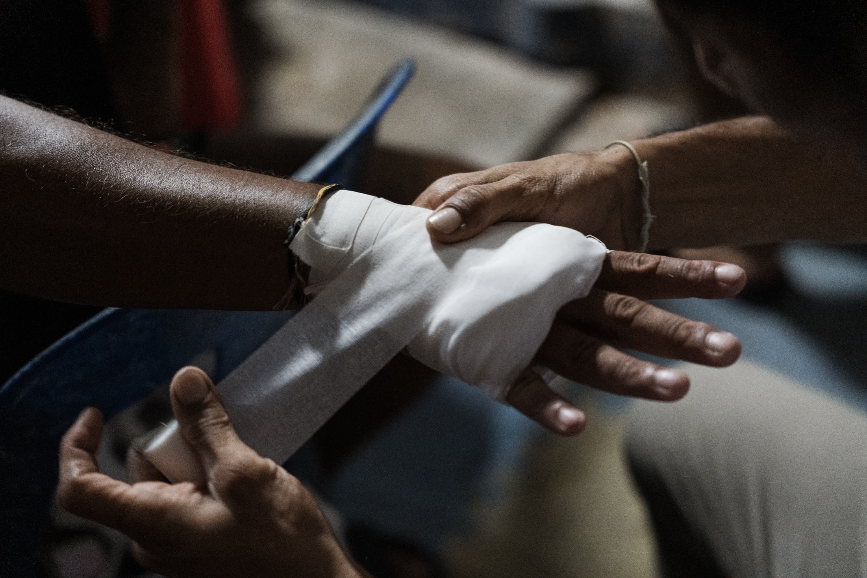 Close-up of hands wrapping a white bandage around another person's wrist and palm.