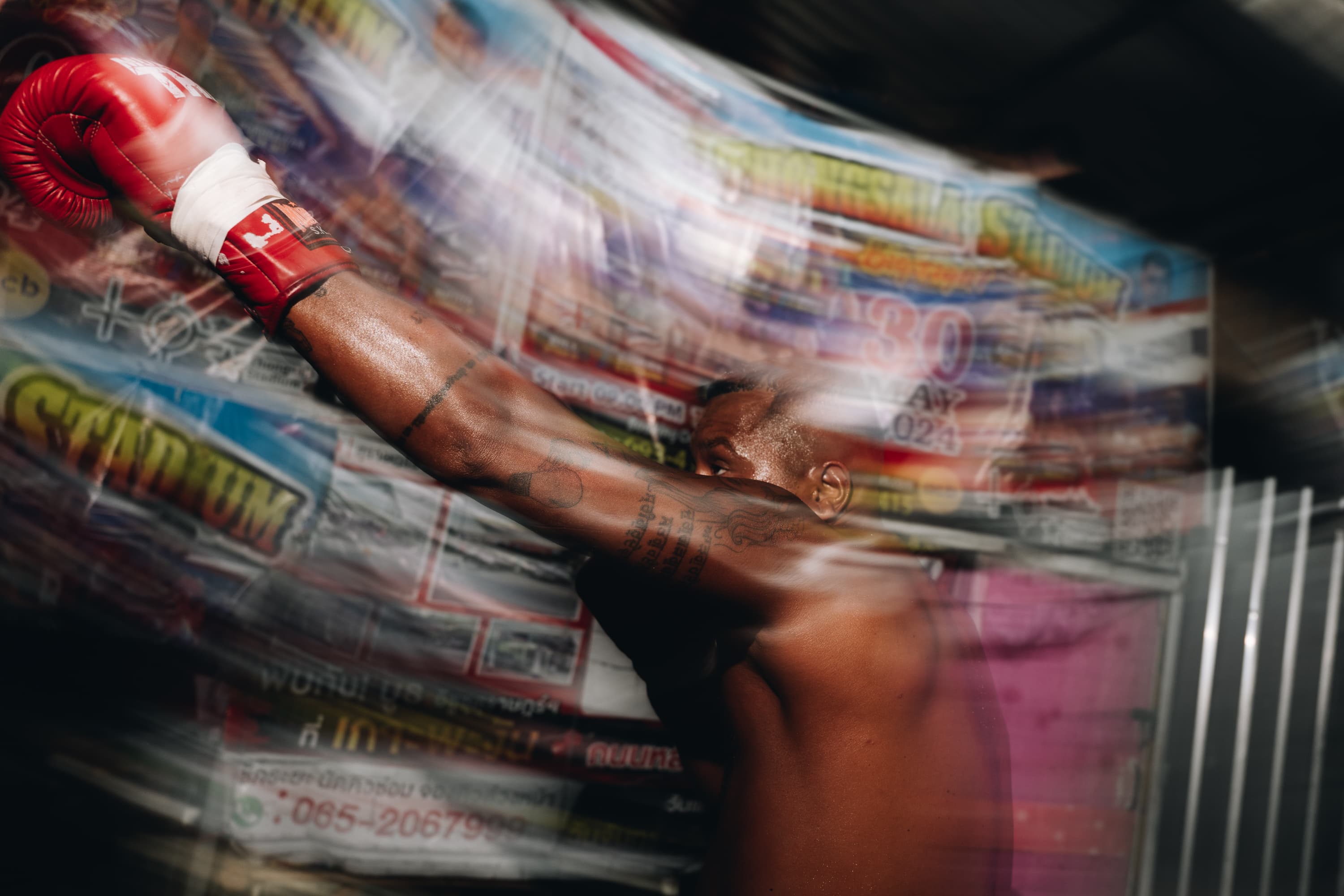 Tattooed boxer throws a punch wearing a red glove behind a blurry, translucent plastic film.