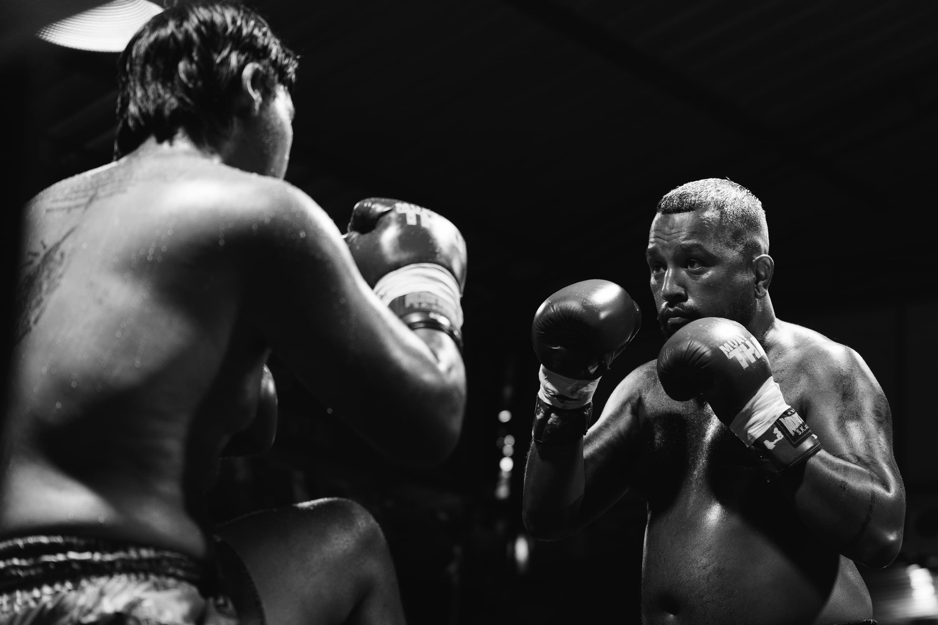Sweaty Muay Thai boxers facing each other in a defensive stance, black and white.