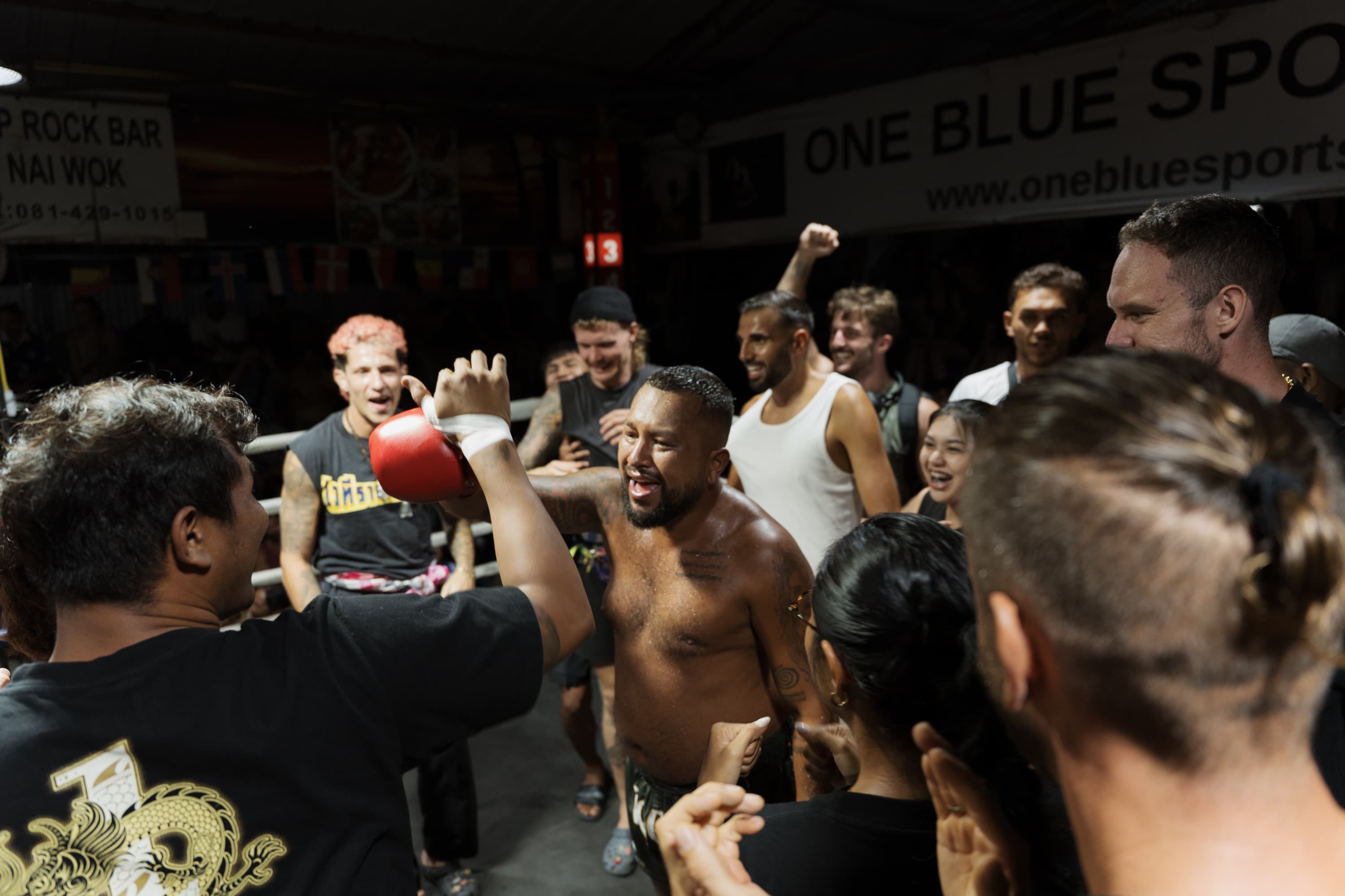 A victorious shirtless fighter celebrates with a cheering crowd inside a boxing ring at night.